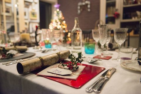 Asztal egy karácsonyi étkezéshez, ezüst és kristálypoharakkal és egy karácsonyfával a háttérben.