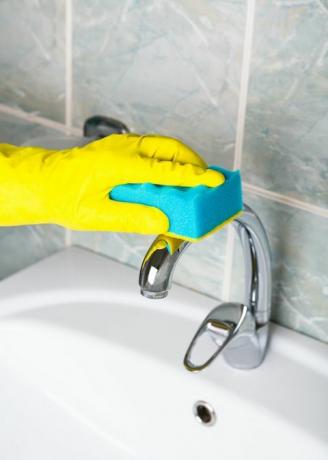 világjárvány fertőtlenítő férfi sárga kesztyűben tisztítja a fürdőszobai csaptelepet, a fürdőkádat és a mosogatószobát pedig sárga védőkesztyűben mossa a piszkos fürdőcsapot vagy mosogató ember kezét, vagy közelről tisztítja a fürdőt