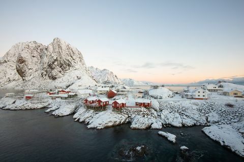 Piros halászati ​​ház falu a hó között, kilátással a hegyekre, a Lofoten-szigeten, Hamnoy Norvégia