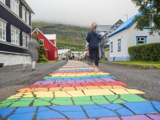 Izland, Seydisfjordur, emberek sétálnak a szivárvány színű aszfaltúton egy félreeső város közepén