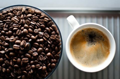 Friss kávébab egy darálóban, egy csésze friss fekete kávé mellett