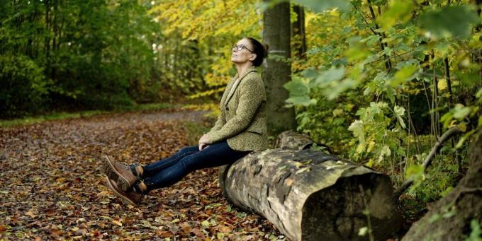 érett nő ül egy fa törzsén egy őszi erdőben
