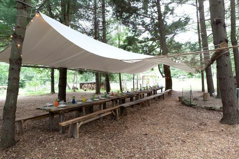 étkezősarok fából készült asztalokkal és padokkal, sátrakkal, ponyvaszerű anyaggal, amelyek az étkező teret szegélyezik